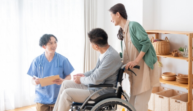 車い椅子に乗った男性を押す女性と、男性の介護士が笑顔で話している様子